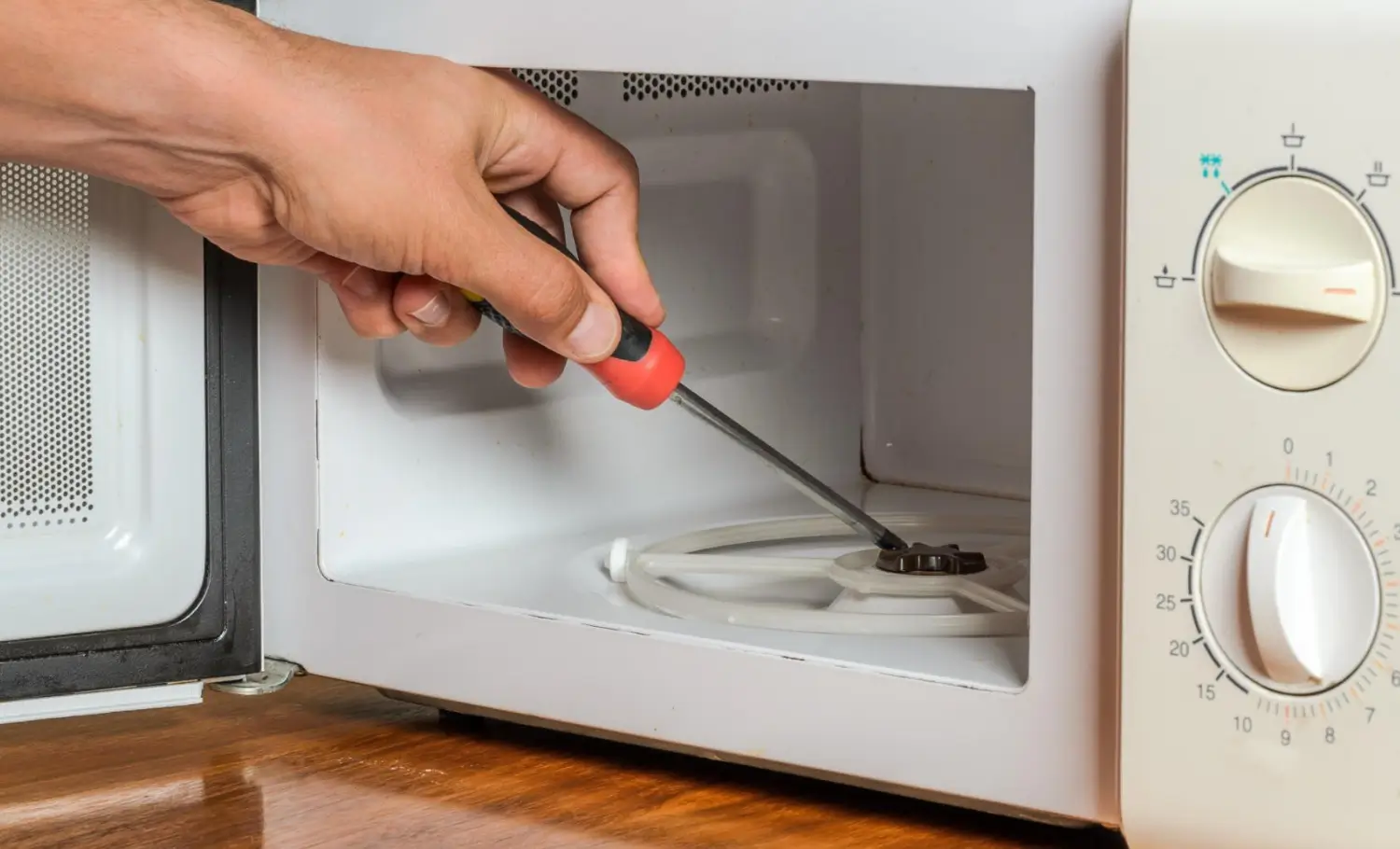 Person fixing microwave with screwdriver.