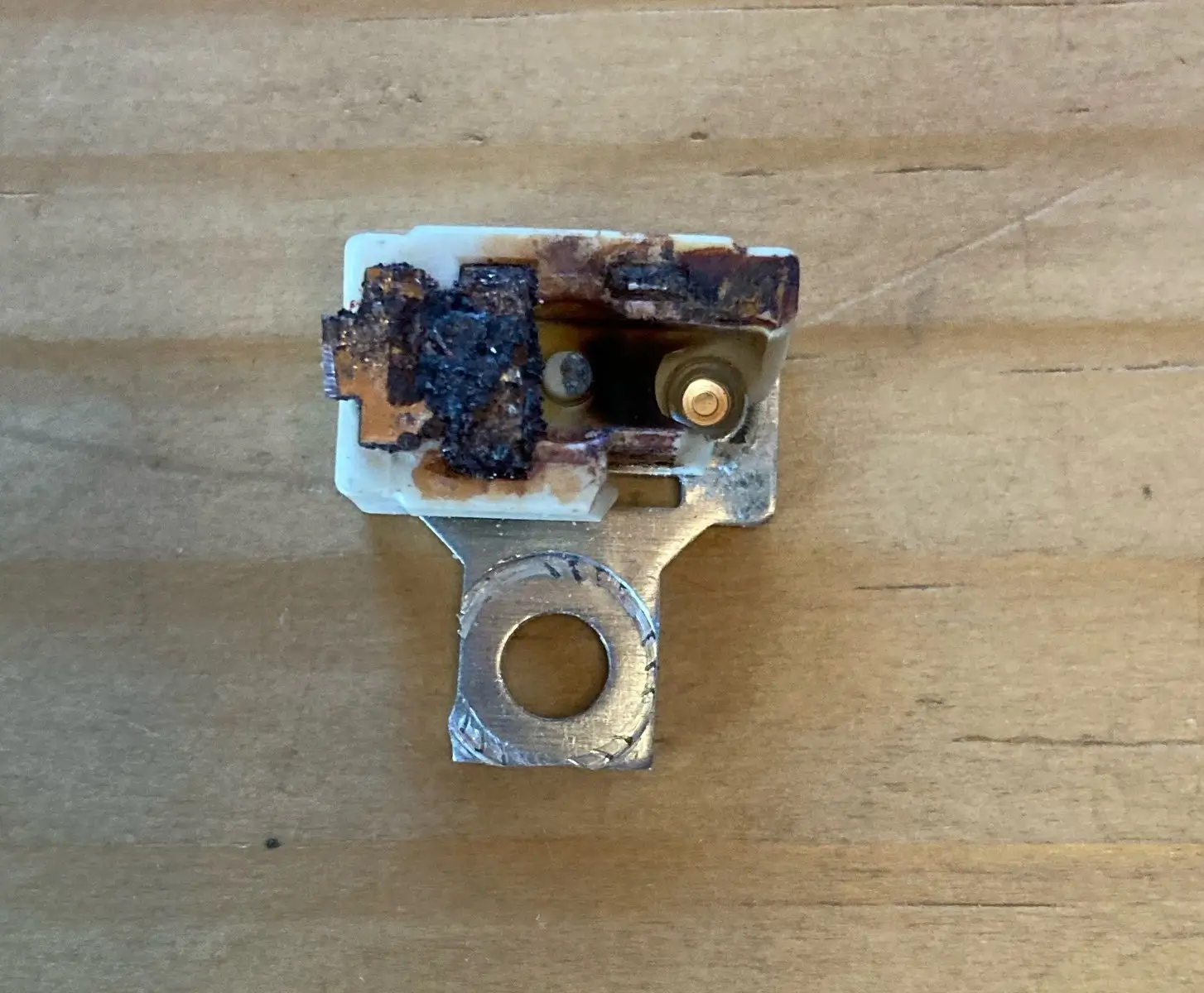 Close-up of a burned electrical switch on a wooden table. The switch is discolored and melted.