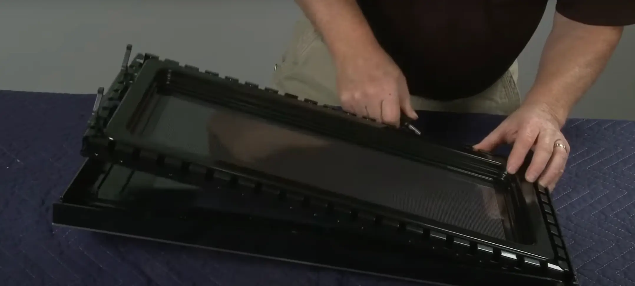 Image of Hands attaching a replacement microwave door by screwing in the hinges.