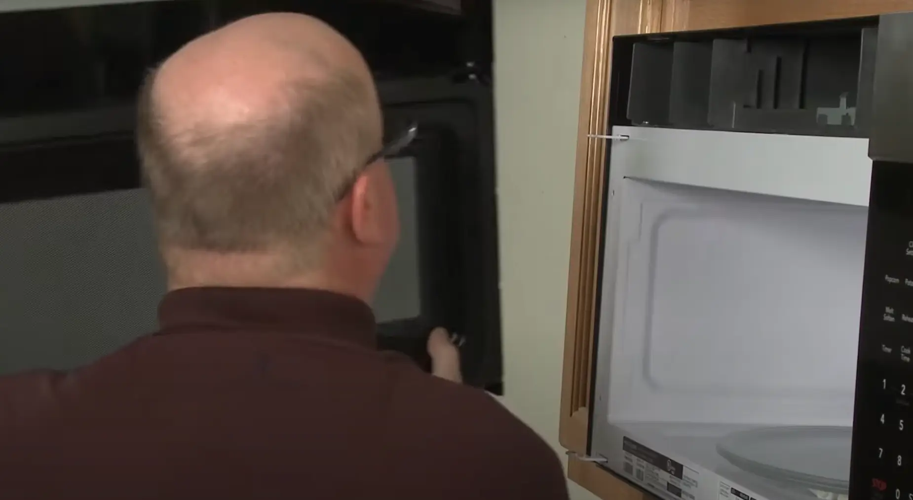 Image of a person removing a broken microwave door by unscrewing hinges.
