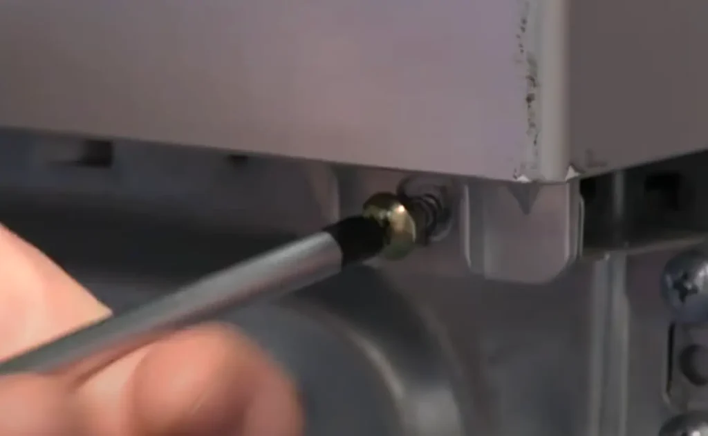A person using a flathead screwdriver to remove a screw from the back panel of a dryer.